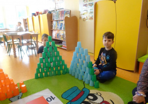 Dwóch chłopców układa z kolorowych kubków plastikowych dwie wieże.